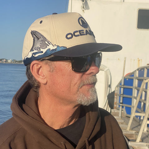 Man wearing natural / navy hat with "OCEARCH" logo on front and shark fin on side