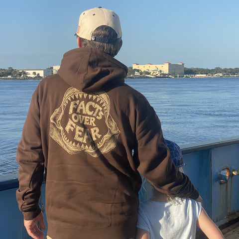 Back view of man wearing brown hoodie with shark jawbone graphic with text "FACTS OVER FEAR"