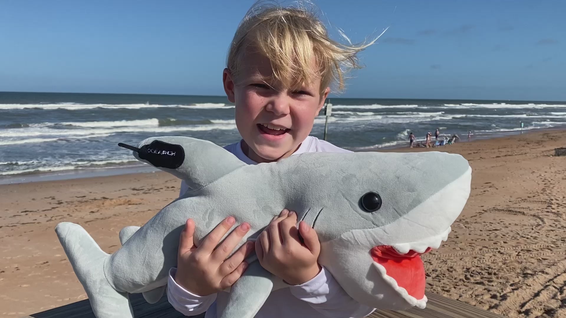 Child holding ocearch shark Plushie saying "Now we have this super soft plushie that everyone can learn and play with at home"